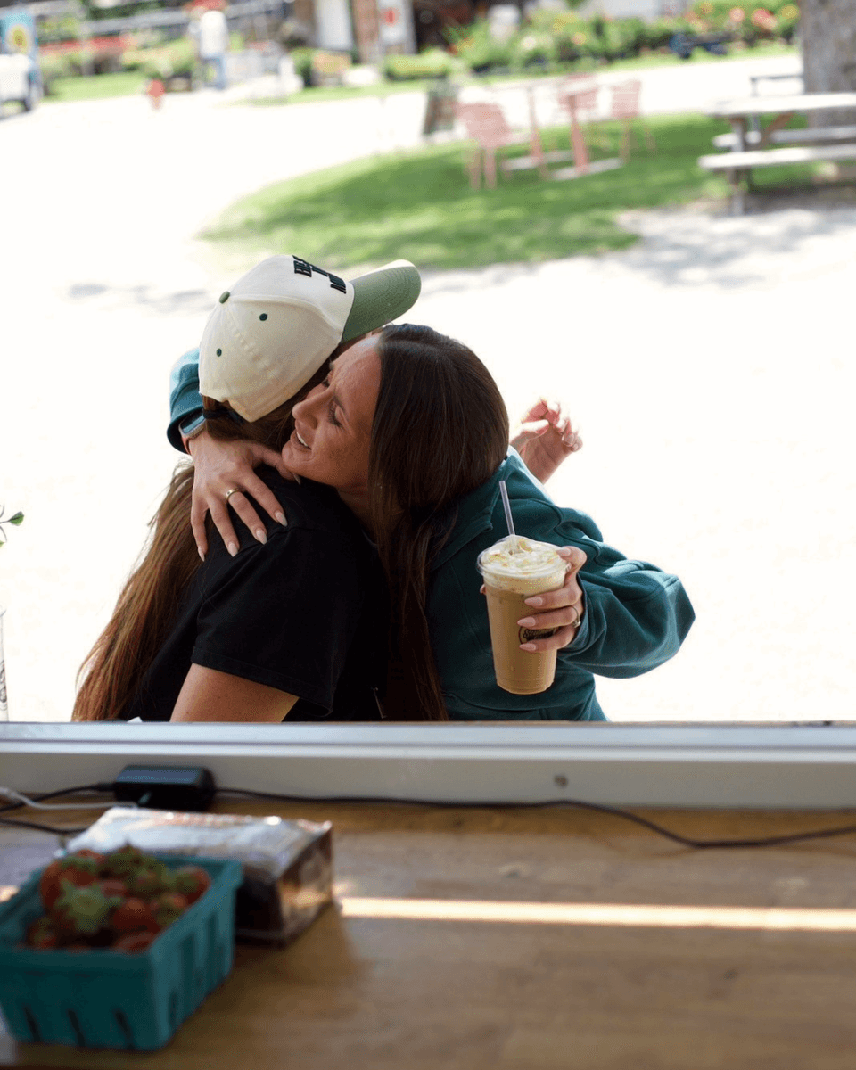 Friends sharing a hug and an iced coffee at the Southern Sips trailer window