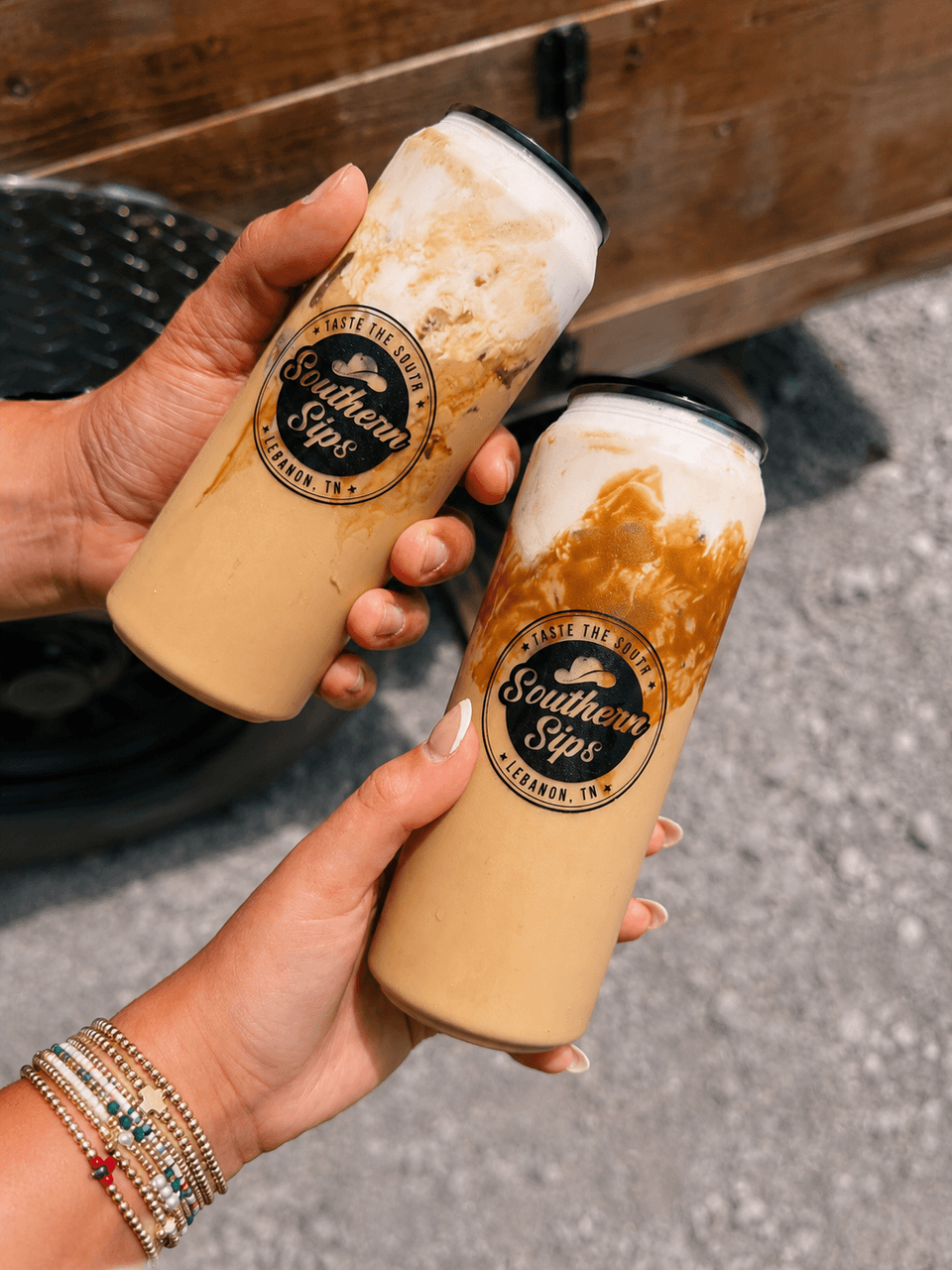 Two Southern Sips canned lattes held up in front of a trailer